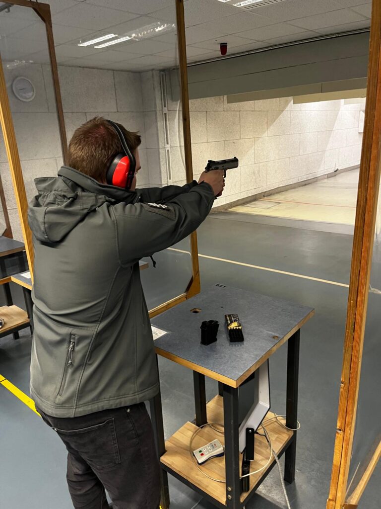 Indoor Schießstand. Schütze zielt mit 9mm Pistole auf 25m.
